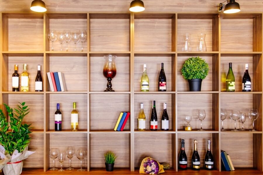 Bottles of white and red wine on a wooden shelf with books in private winery cabinet room interior